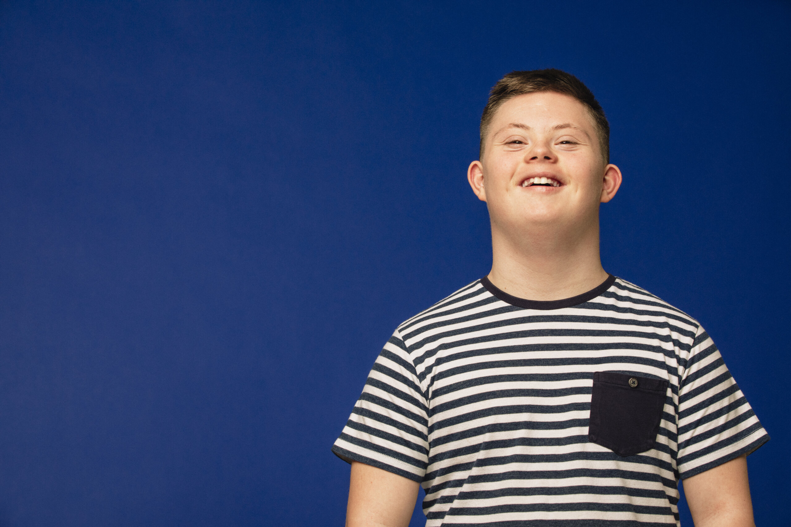 Image of a teenage down syndrome boy looking at the camera, smiling and looking happy