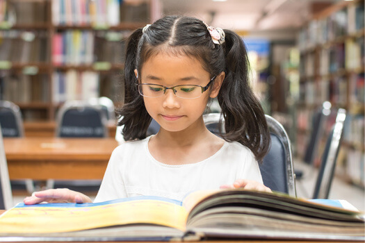 young girl with pigtails reading at a library table