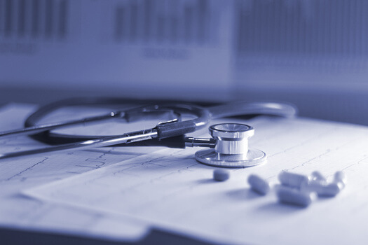 black and white photo f a stethescope laying on medical records. with capsules of medication next to it.