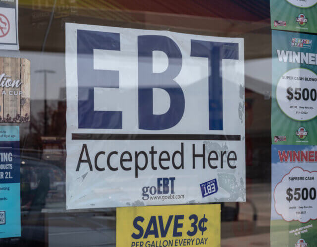 A storefront window displaying a large EBT Accepted here sign in the center of smaller ads